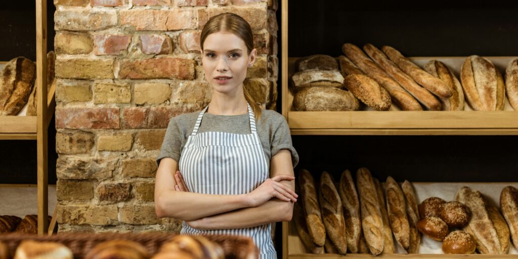 beautiful young baker with crossed arms standing at pastry store