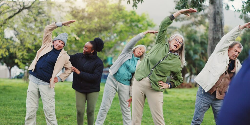 Yoga class, park and elderly group with coach exercise together in nature for health and wellness t