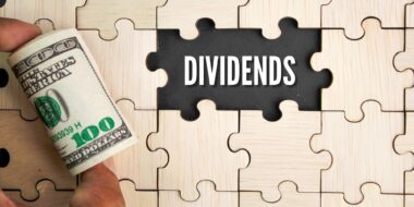 wooden puzzle and a roll of paper money with the word dividends.