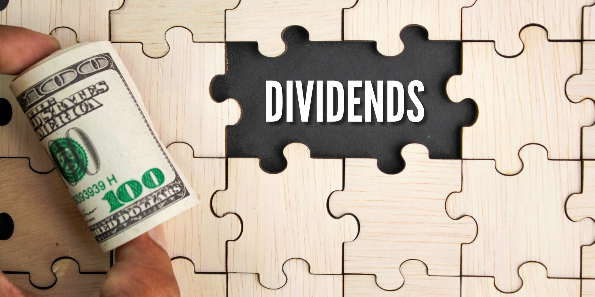 wooden puzzle and a roll of paper money with the word dividends.
