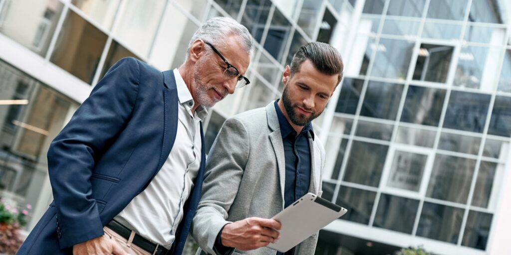 Young and senior business men using digital tablet outdoors on the city background