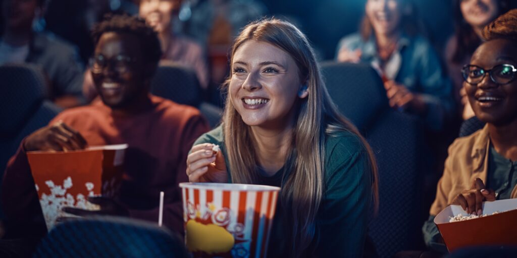 Young happy woman watching movie and eating popcorn at cinema.